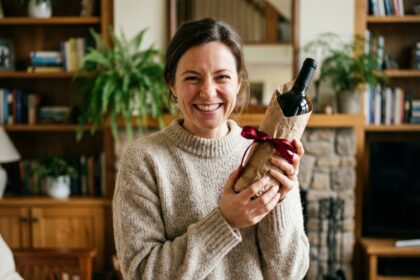 Femme souriante tenant un cadeau vin dans un salon chaleureux
