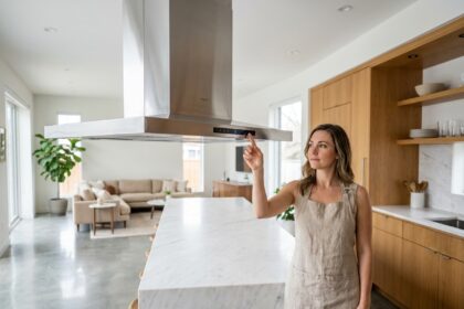 Femme examinant une hotte aspirante suspendue en inox au-dessus d'un îlot de cuisine dans un espace cuisine-salon ouvert moderne